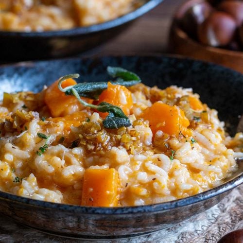 A bowl of instant pot pumpkin risotto in a black bowl topped with brown butter chestnut sauce and fried sage leaves.