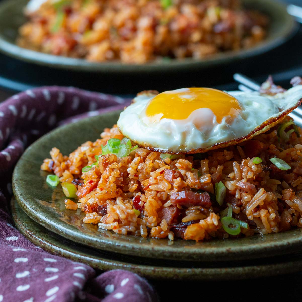 2 plates of gochujang rice topped with a sunny side up fried egg.