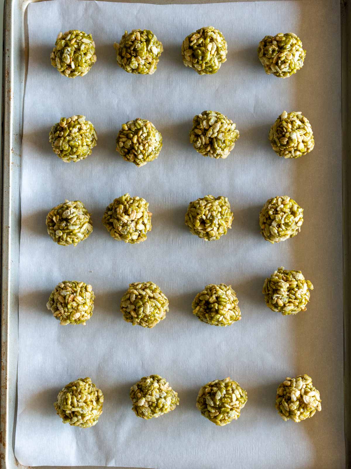 Rolled matcha crispy rice cereal ball treats laid out on a baking sheet.