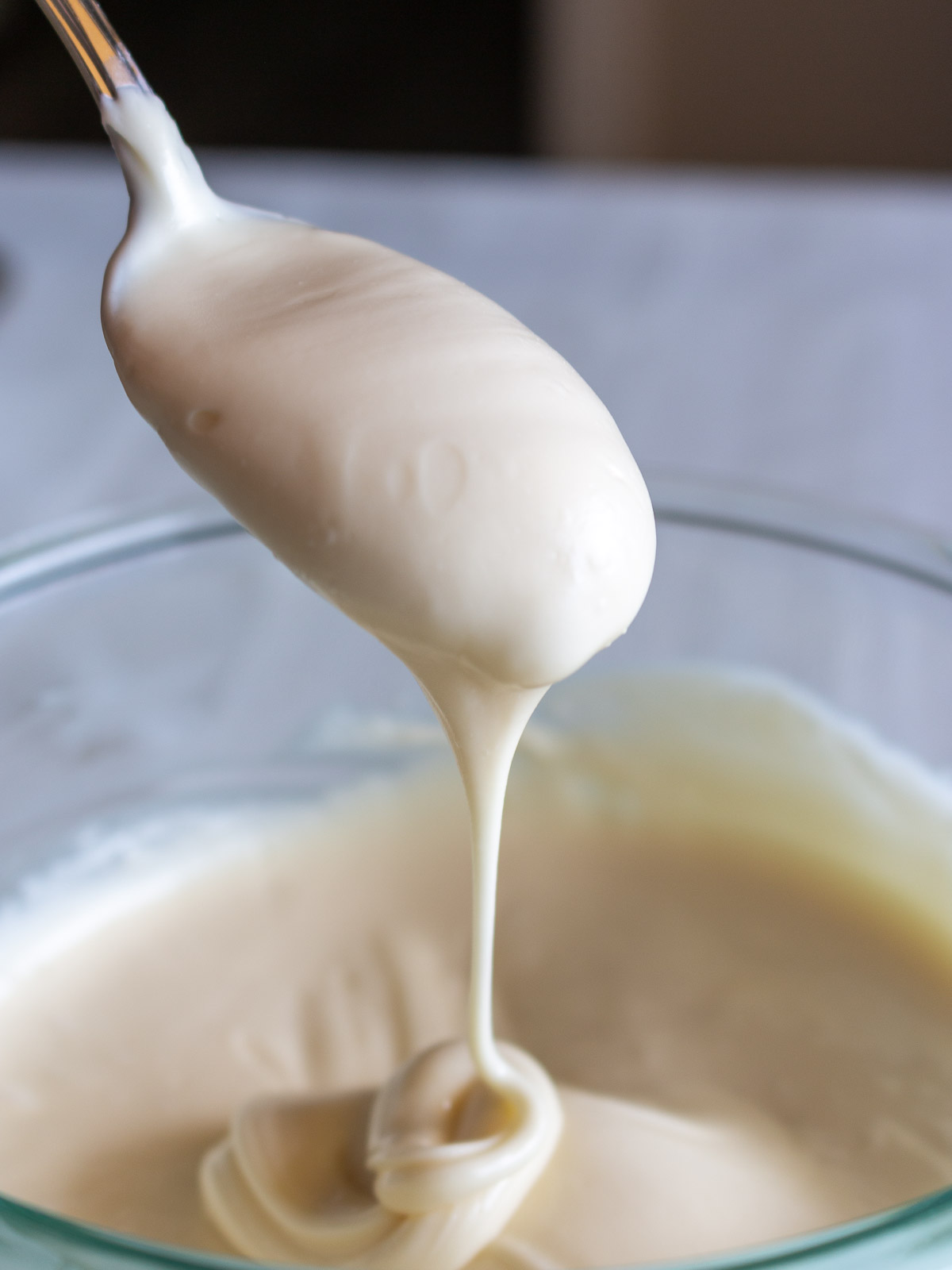 Melted white chocolate dripping from a spoon into a clear bowl.