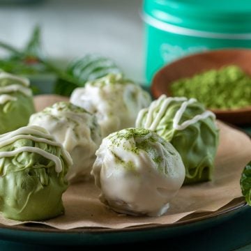 Chocolate matcha crispy truffles decorated with white chocolate drizzle and a dusting of matcha powder on a decorative tan plate.