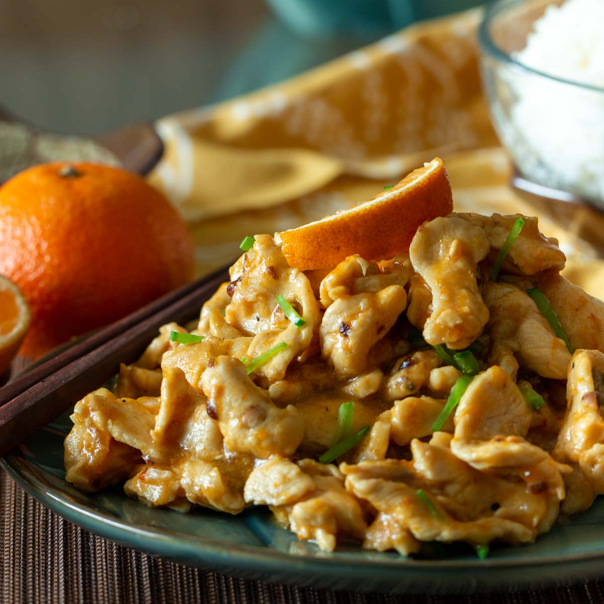Stir fried hot and spicy mandarin orange chicken on a blue plate garnished with oranges and green onions.