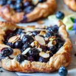 Hot out of the oven blueberry tarts with puff pastry on a lined baking sheet.