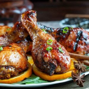 Tea smoked chicken legs on a plate garnished with oranges.