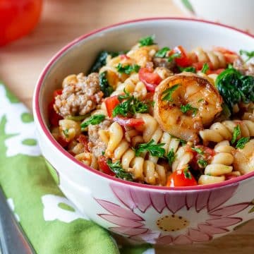 Shrimp and sausage pasta in a flowered bowl with a green napkin.