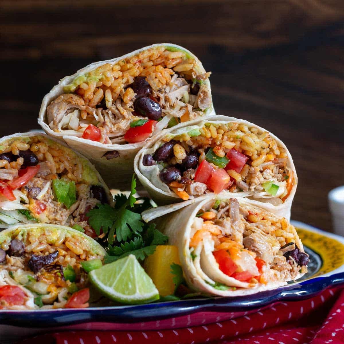 Pork carnitas burritos piled up on a plate with pineapple slaw and all the fixings.