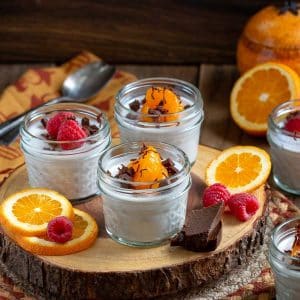 3 jars of spicy chai coconut jelly on a wooden wheel garnished with oranges, raspberries and chocolate.