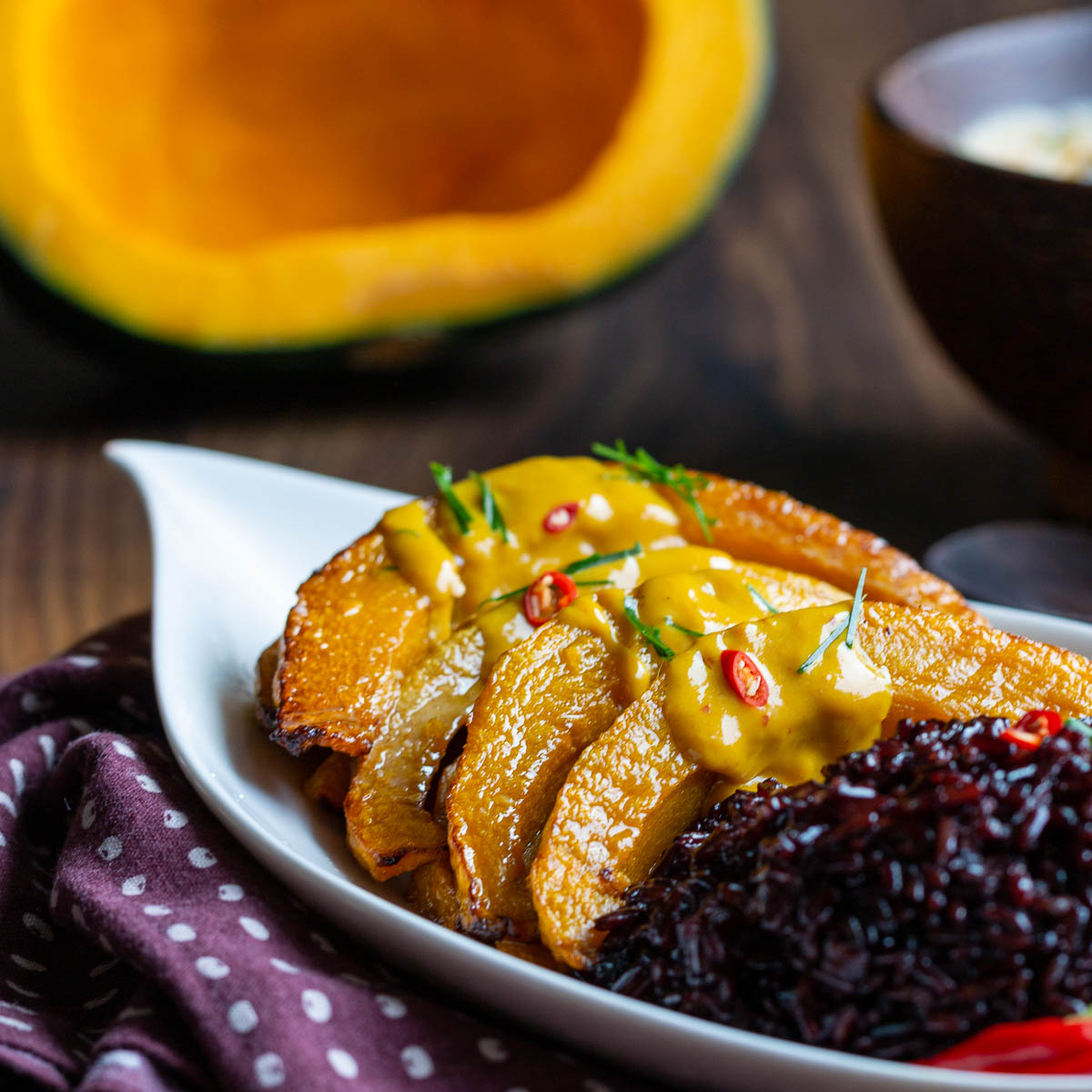 Roasted air fryer kabocha squash with Thai curried sauce on top in a white plate served with black rice.