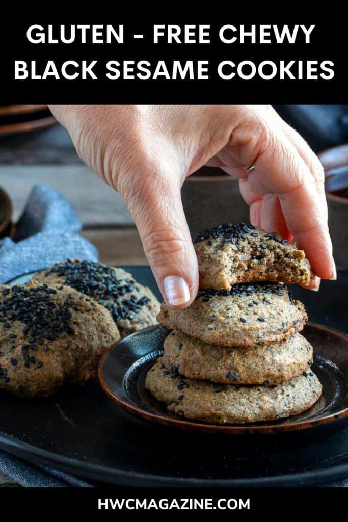 Hand picking up a black sesame cookie with a bite out of it.