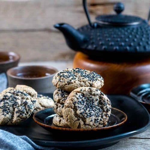 Chewy gluten free black sesame cookies on a black plate served with tea.