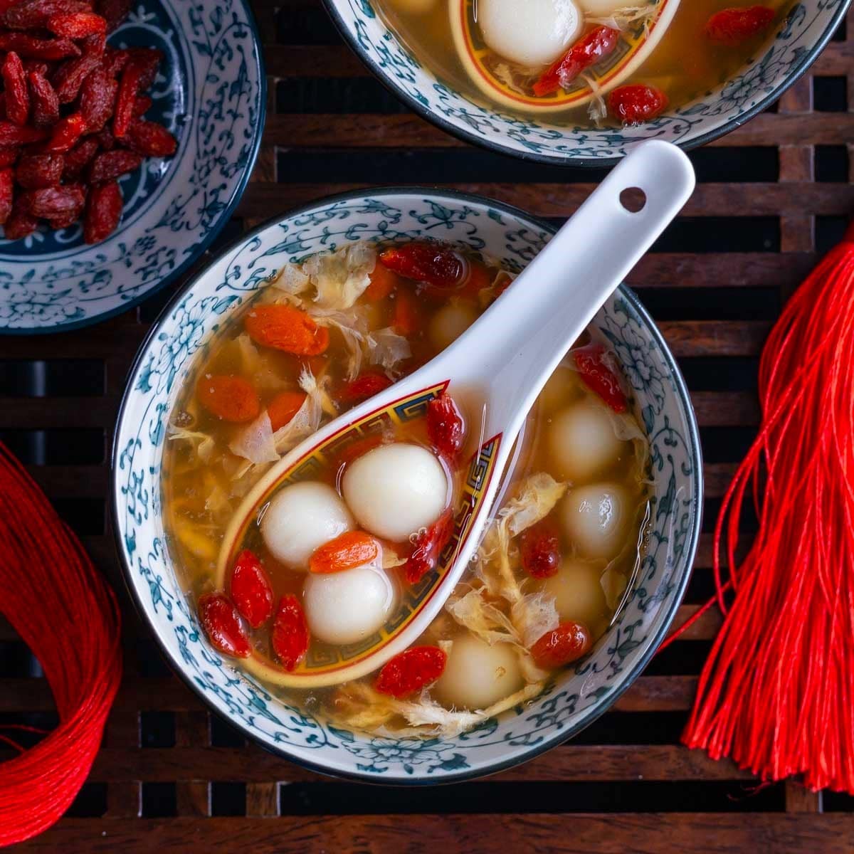 Glutinous rice balls in a spoon in the osmanthus sweet soup broth in a blue bowl.