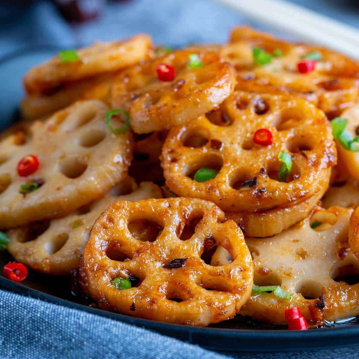 Spicy Lotus Root Stir Fry on a black plate garnished with chili and green onions.