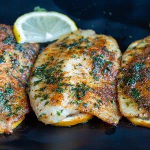 Cooked air fryer frozen fillets on a black plate with lemon wedges.