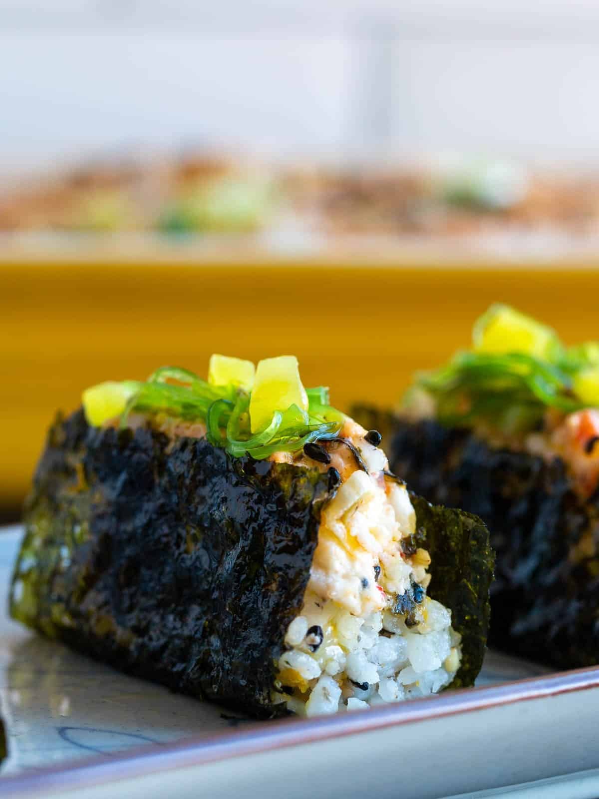 Close up of a prepared sushi baked wrapped up in nori with toppings. 