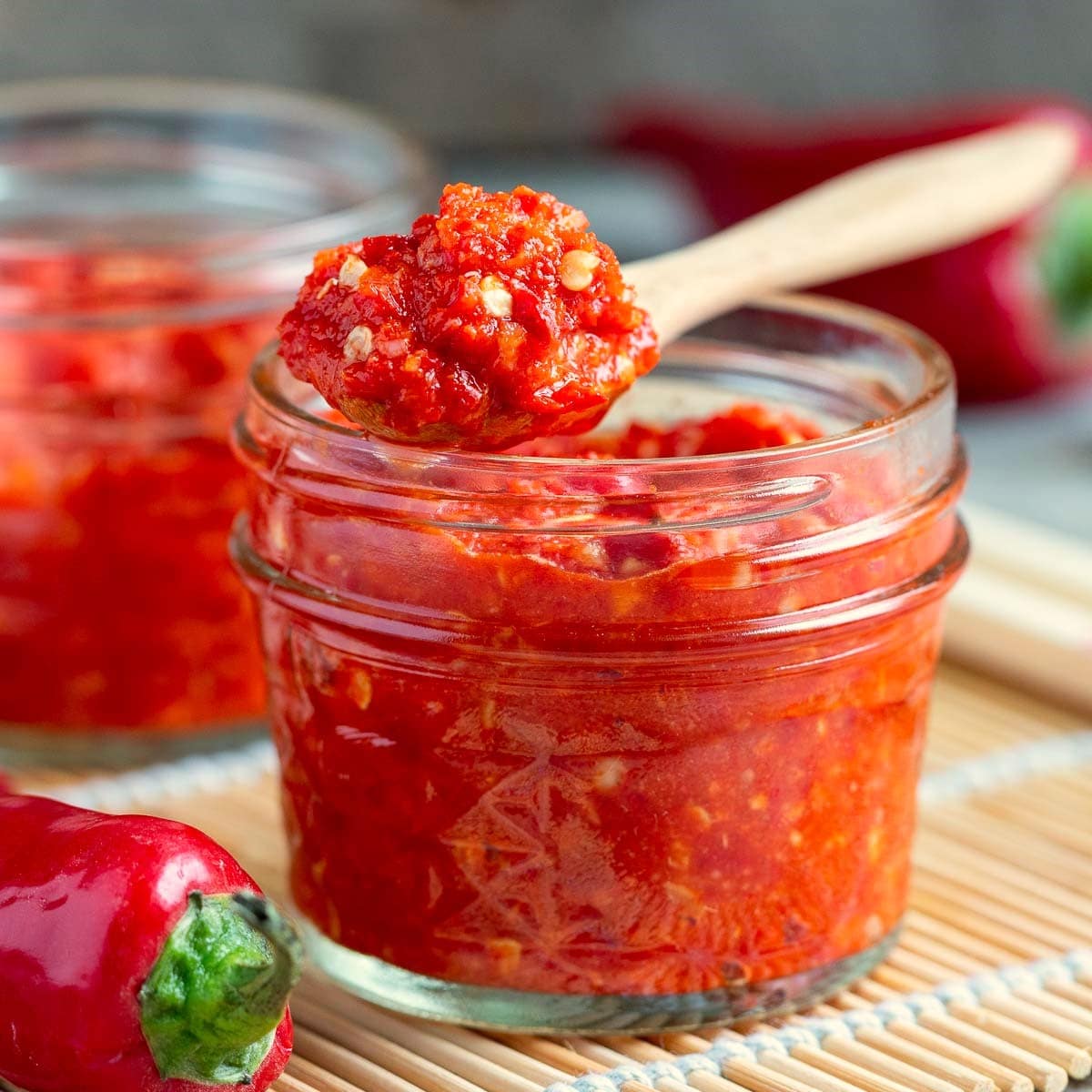 2 jars of thick Asian Chili garlic sauce with a scoop on a wooden spoon.