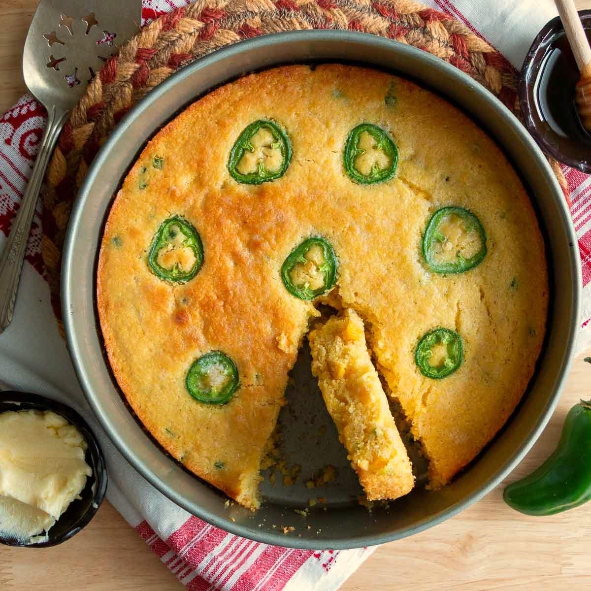 Freshly air fried jiffy cornbread in a cake pan with a slice showing how moist it is.