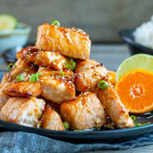 Orange glazed air fryer salmon bites piled high on a black plate served with rice.
