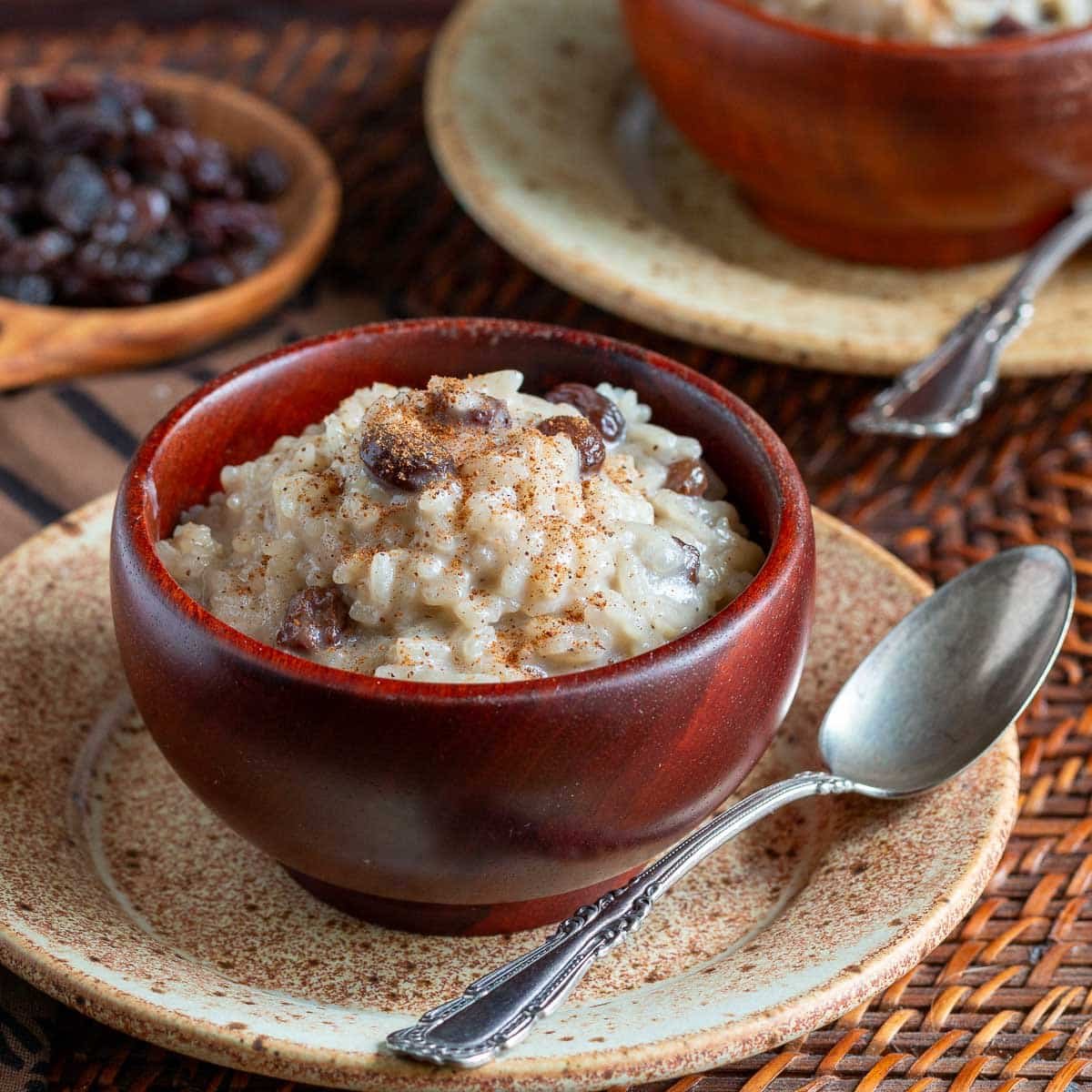 Coconut rice pudding made with condensed milk in a wooden bowl with a sprinkle of cinnamon and raisins.