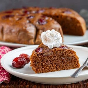 Steamed gingerbread date bread on a white plate garnished with a dollop of non-dairy cream and jujubes.