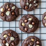 Fudgy dark chocolate macadamia nut cookies hot out of the oven resting on a cooking rack.