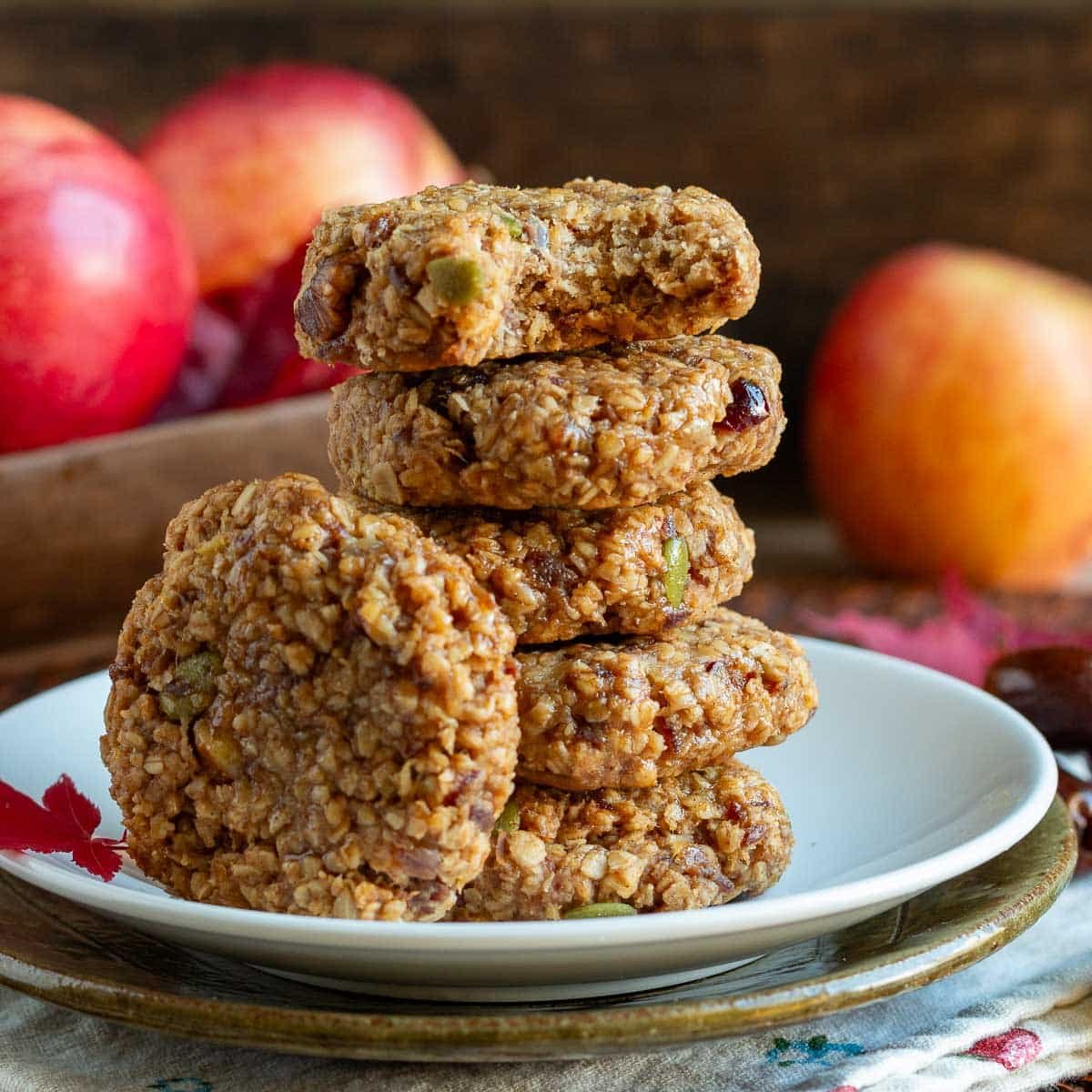 Apple oatmeal date cookies stacked on white plate with a bite out of one.