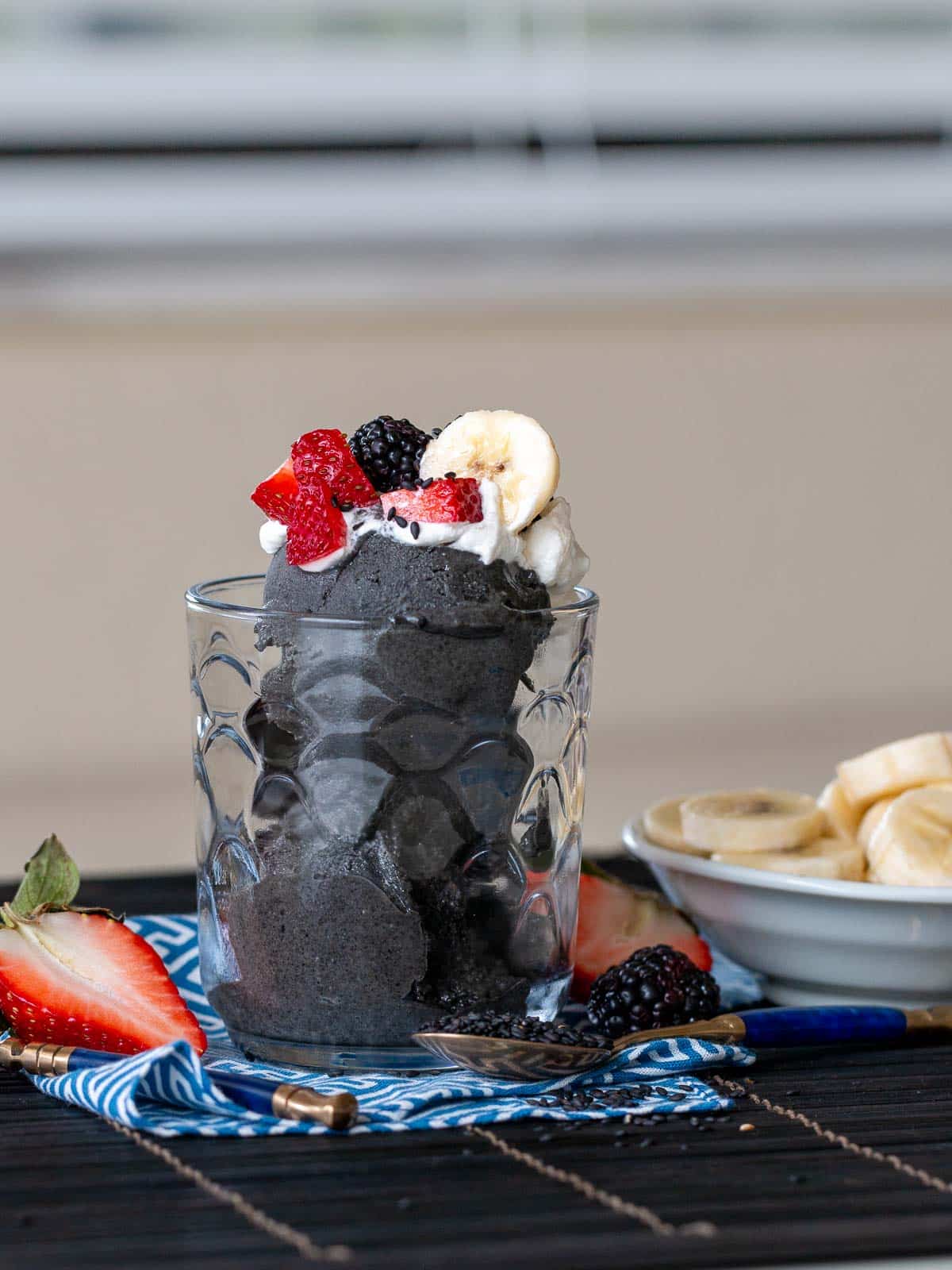 3 scoops of black sesame ice cream in a clear glass garnished with fruit and sesame seeds. 