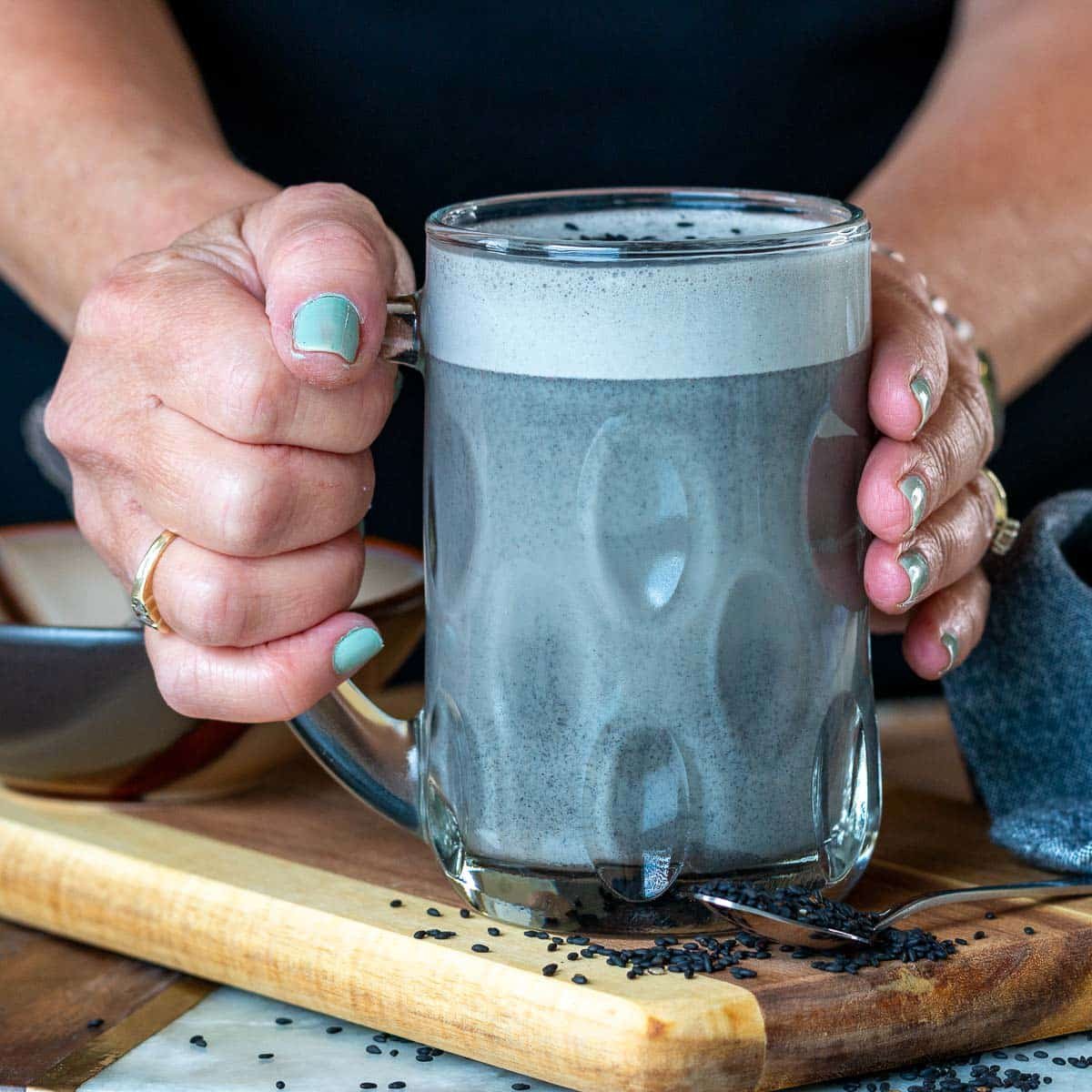 Holding a clear mug of hot black sesame latte.