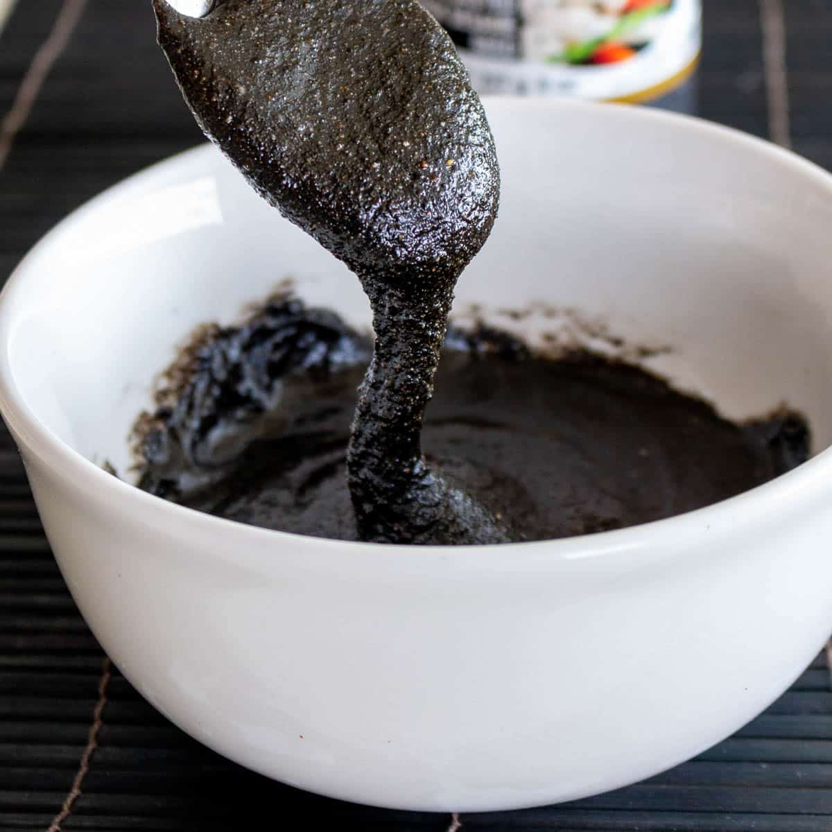 Homemade black sesame paste thick and slowly flowing from a spoon onto a white bowl.