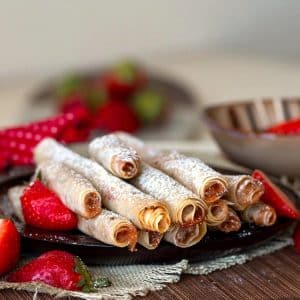 Crispy strawberry jam roll cookies on a brown plate topped with powdered sugar.