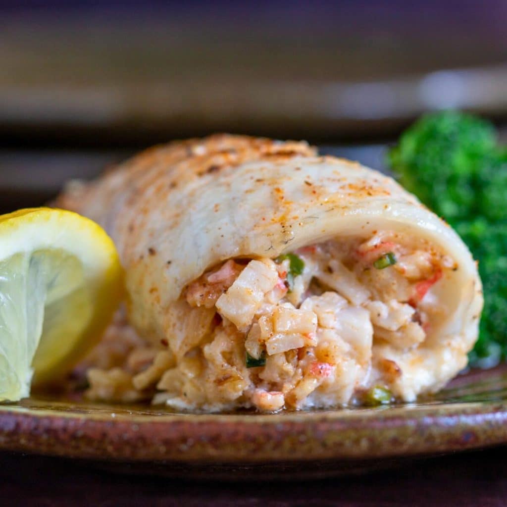 Crab stuffed whitefish recipe with lemon on a brown plate.