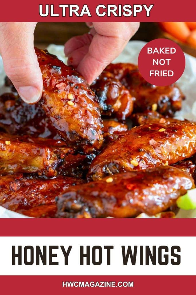 Honey hot wings getting grabbed off a wooden plate lined with parchment paper.