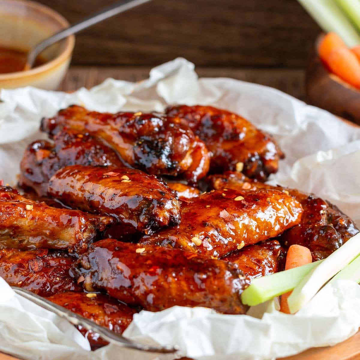 Baked honey hot wings in a plate lined with parchment paper and extra sauce on the side.