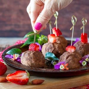 Holding a no bake strawberry chocolate cheesecake bite on a fancy serving plate with styled toothpicks.