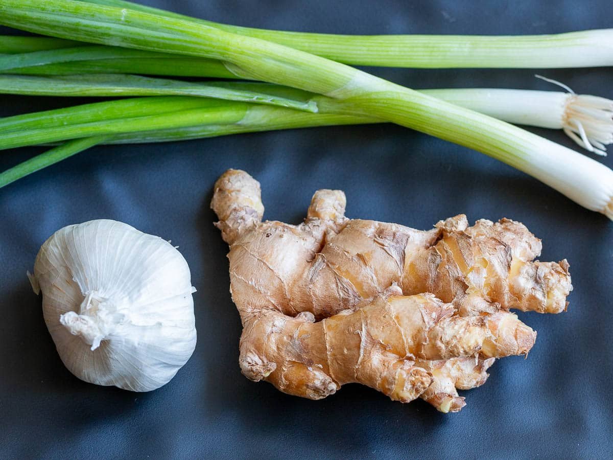 Garlic, green onion and ginger on a black plate.