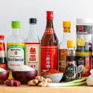 Many essential Asian pantry staples sitting out on a wooden table.