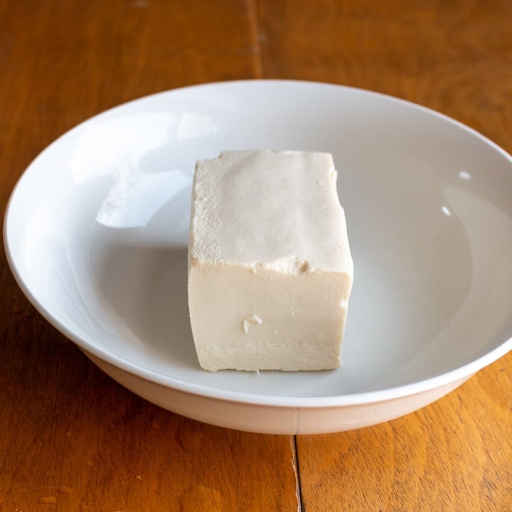 Half of a block of firm tofu in a white bowl.