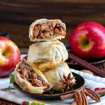 Apple pecan spring roll mooncakes stacked on a plate with one cut in half showing the delicious apple pie filling.
