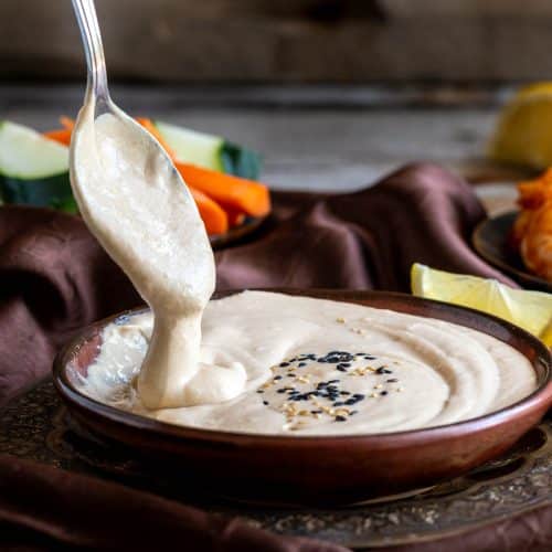 Spoon of Tarator sauce in brown bowl showing how thick and creamy it is.