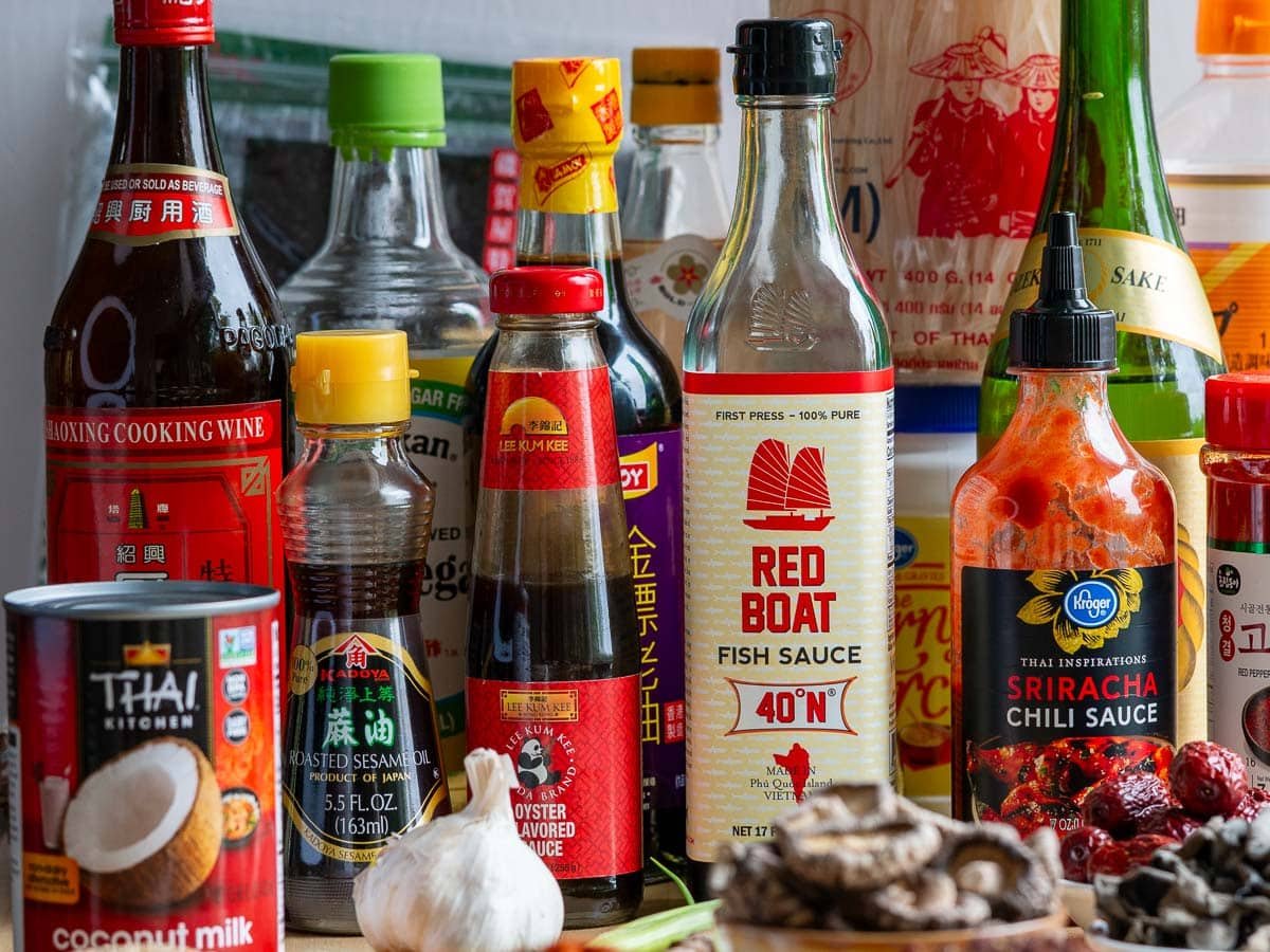 Many different kinds of Asian sauces in bottles stacked on the table. 