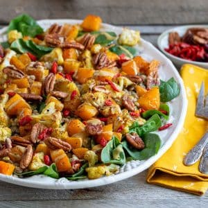 Warm curried autumn salad with roasted butternut squash and cauliflower with a creamy tahini maple dressing on a white platter.