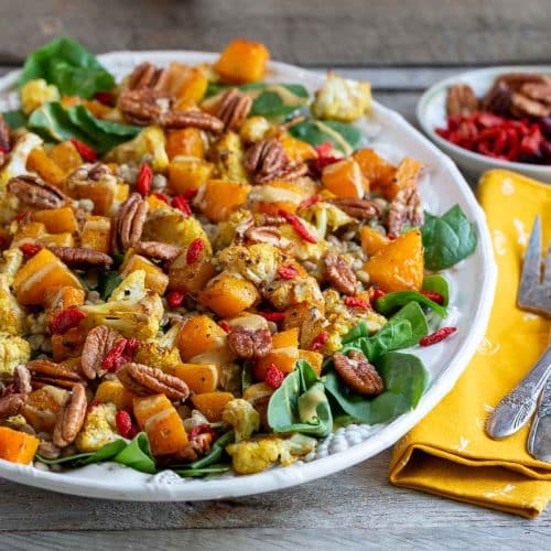 Warm curried autumn salad with roasted butternut squash and cauliflower with a creamy tahini maple dressing on a white platter.