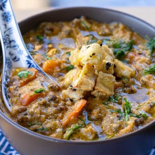 Hearty protein packed mung bean soup with coconut milk topped with crispy tofu croutons in a brown bowl.