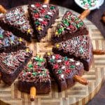 Christmas tree sweet potato brownies decorated with sweet potato frosting and pretzel stems on a round wooden cutting board.