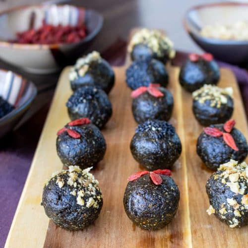 Black sesame walnut bliss balls garnished with goji berries and placed on a wooden board.