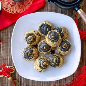 Black sesame pie crust pinwheel cookies on a white plate with Chinese New Year Decorations and tea.