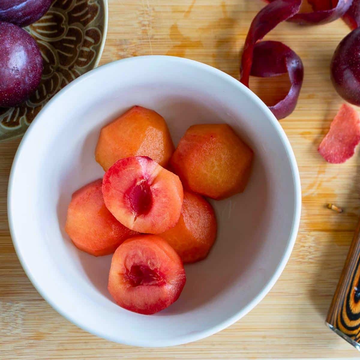 Peeled fresh plums cut in half in a white bowl.