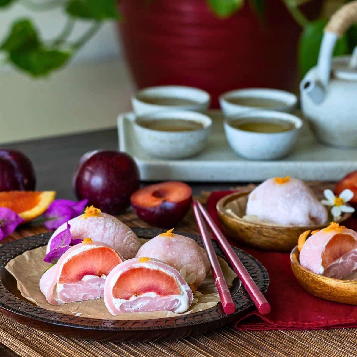Teatime scene with Japanese plum daifuku soft mochi cut in half showing the orange coconut cream filling and fresh plums. 
